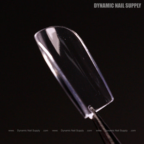 A Natural Square (Short) Full Cover Soft-Gel Nail Tip is held by tweezers against a black background.