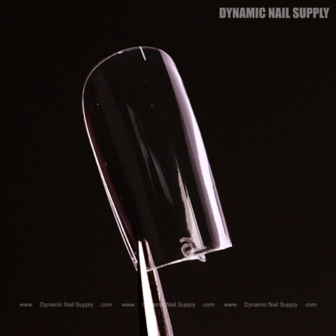 A Natural Square (Short) Soft-Gel Nail Tip (Pink Box) held by tweezers against black with “DYNAMIC NAIL SUPPLY.”.