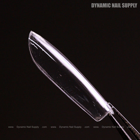 A Natural Square (Short) Full Cover Soft-Gel Nail Tip held by tweezers, shown against a black background.
