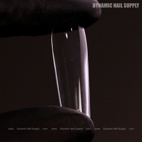 A gloved hand holds a Natural Square (Long) Full Cover Soft-Gel Nail Tip (Pink Box) against a dark background.