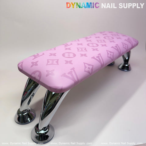 The (Big Logo Pink LV Pattern) Leather Armrest Cushion Pillow for Pedicure Manicure by Dynamic Nail Supply features a monogram pattern that echoes luxury branding. It includes four curved, reflective chrome legs and comes with a built-in UV nail light. The product is displayed against a plain white background, with the Dynamic Nail Supply text appearing at both the top and bottom borders.