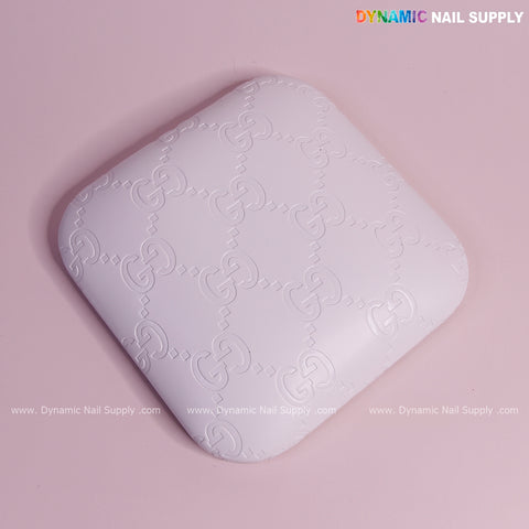 The (White GC Engrave - Smooth) Elbow Pad Pillow for Nail Tech rests on a pink surface; soft PU leather, supportive.