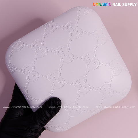 A gloved hand holds the White GC Engrave - Smooth Elbow Pad Pillow for Nail Tech on a pink background.