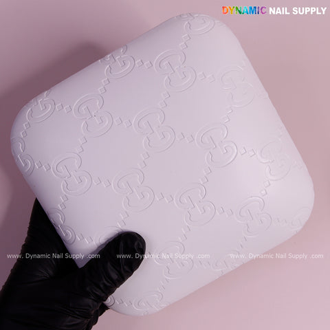 A gloved hand holds the White GC Engrave - Smooth Elbow Pad Pillow for Nail Tech on a light pink background.