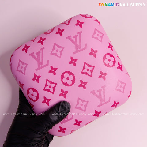 A gloved hand holds the Pink and Pink LV Smooth Leather Elbow Cushion Pad Arm Rest Support for a manicure nail desk.