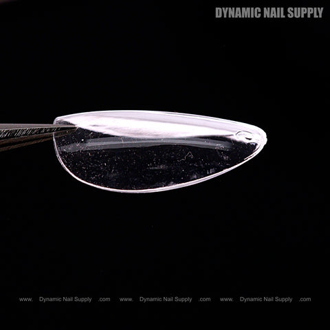 A close-up of tweezers holding a Natural Almond (Short) Full Cover Soft-Gel Nail Tip against a black background.