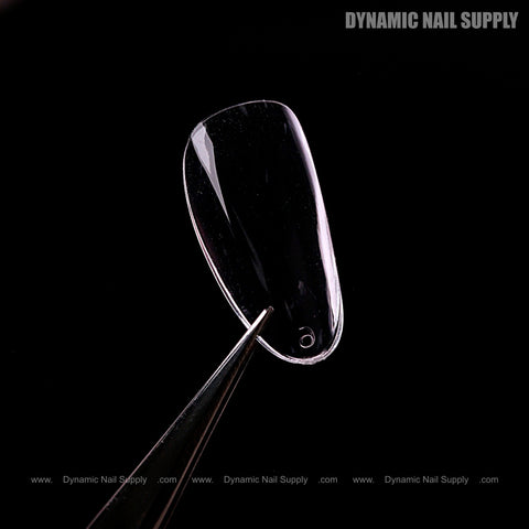 A Natural Almond (Short) Full Cover Soft-Gel Nail Tip in Pink Box is held by tweezers against a black background.