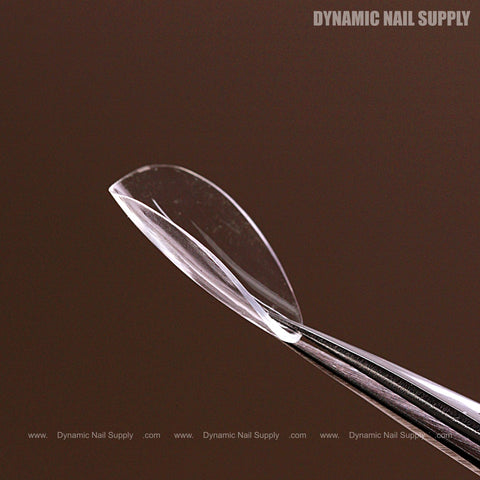 A Natural Almond (Short) Full Cover Soft-Gel Nail Tip held by tweezers, “Dynamic Nail Supply” in the corners.