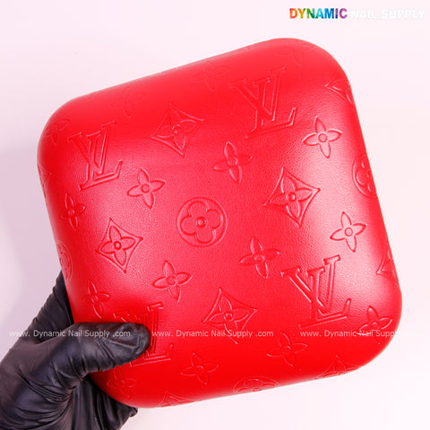A gloved hand holds the Red LV Engrave Elbow Pad for Nail Tech—soft PU leather, supportive—against a pink background.