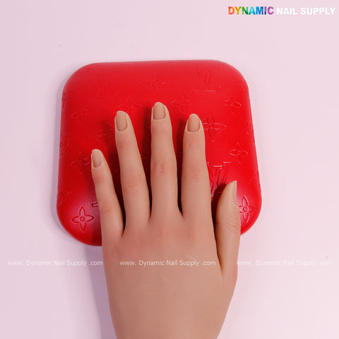 A mannequin hand with nude nails rests on the Red LV Engrave Elbow Pad for Nail Tech against a light pink background.
