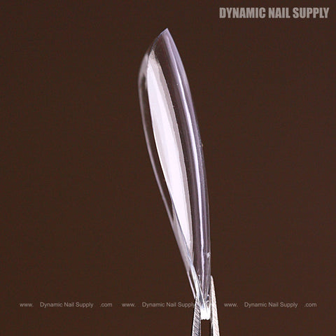 A Natural Almond (Long) Full Cover Soft-Gel Nail Tip held upright by tweezers against a plain brown background.