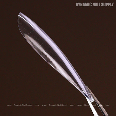A Natural Almond (Long) Full Cover Soft-Gel Nail Tip held by tweezers against a dark brown background.