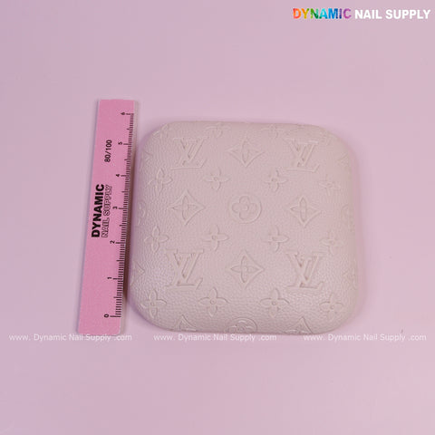 A pink ruler beside a White LV Engrave-Grain Elbow Rest Pad for Nail Tech on a pink background.