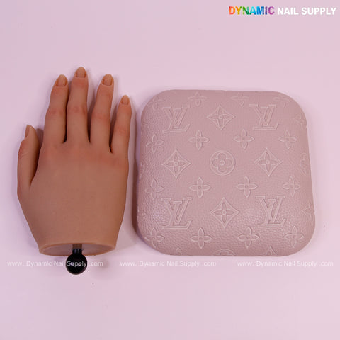 A lifelike practice hand and a Neutral skin Color LV Engrave elbow pad pillow for nail techs on a pink background.