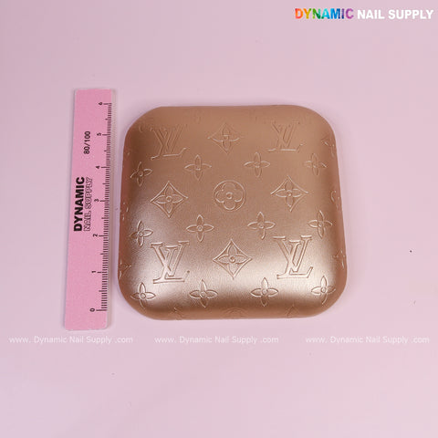 A pink ruler next to a Metallic Gold LV Engrave Elbow Rest Pillow for Nail Tech on a light pink background.