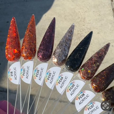 A close-up of nine pointed nail polish swatches on clear sticks showcases the "Flavors Of Fall" 2024 Acrylic Powder Collection from Dynamic Nail Supply. The collection features a variety of long-lasting fall-themed colors, ranging from bright orange to dark brown, with glittery finishes. Each stick is labeled with a unique code and the word ACRYLIC in bold, while sunlight accentuates the sparkles.