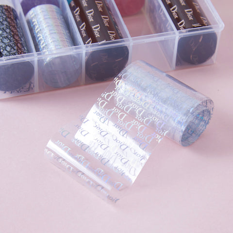 Nail Art Design Foils - Luxury Style with repeating Dior logo, perfect for chic nails, unrolled on a pink surface.