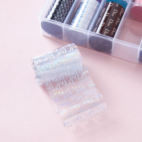 Nail Art Design Foils - Luxury Style shown with a clear foil featuring iridescent Dior logos on a pink background.