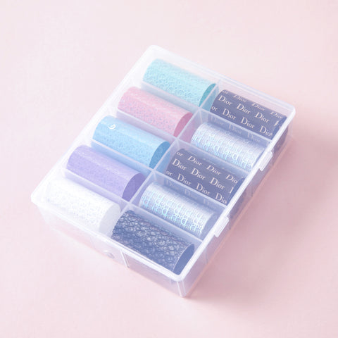 A plastic box holds ten Luxury Style Nail Art Design Foils, some labeled Dior, displayed on a pink surface.