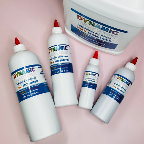 Four bottles with white labels and a large container of Dynamic Nail System Monomer – EMA Nail Liquid by Dynamic Nail Supply are displayed on a light pink surface. Each bottle, perfect for mixing with Acrylic Powder, is topped with a red cap and features the vibrant Dynamic logo alongside product details on the label. The available sizes vary from small to large.