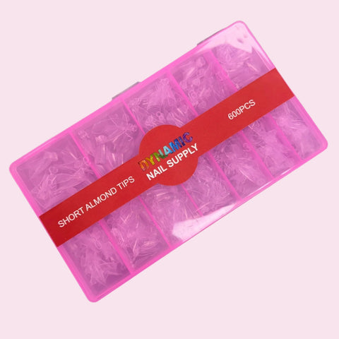 A pink plastic box containing 600 short stiletto almond nail tips, neatly organized into compartments. A red band across the middle displays DYNAMIC NAIL SUPPLY and SHORT ALMOND TIPS 600 PCS. The light pink background adds an elegant touch to the presentation.