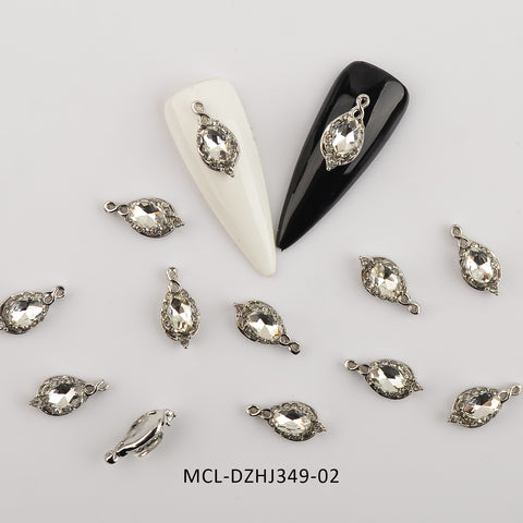 Dynamic Nail Supply presents two long, oval-shaped nail tips, featuring one in white and the other in black, each embellished with a teardrop-shaped rhinestone charm. Beneath them lie eleven similar silver charms of unique shapes scattered on a pristine white background. At the bottom is the text MCL-DZHJ349-02. Ideal for innovative nail designers seeking to elevate their art with Dynamic Nail Supply's 20 pcs/bag of Unique Shape Charms for Nail Art Design.