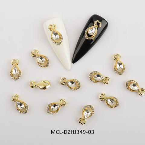 Gold and rhinestone teardrop nail charms are beautifully arranged on a white background, highlighting two charms on black and white nail tips. Each charm features a clear teardrop stone surrounded by smaller rhinestones, making them perfect for nail designers. Dynamic Nail Supply offers this pack of 20 unique shape charms for nail art design under the code MCL-DZHJ349-03.