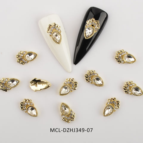 A close-up view features assorted teardrop-shaped nail charms from Dynamic Nail Supply, each adorned with gold, rhinestones, and small clear crystals. Two long, pointed nail tips—one in white and the other in black—exhibit these unique shape charms designed for nail art. The background is a plain white, with the product code MCL-DZHJ349-07 shown at the bottom. Each bag contains 20 pieces of these distinctive charms.