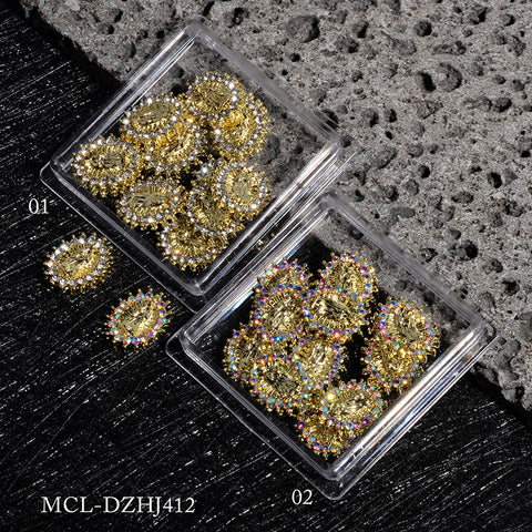 On a textured black and gray surface, two clear boxes from Dynamic Nail Supply hold ornate gold Virgin Mary charms for religious nail designs. The first box, containing the small version labeled 12 pcs bag (01), has one charm placed beside it, while the second (02) is fully stocked. Each charm showcases intricate details with colorful rhinestones bordering the edges.