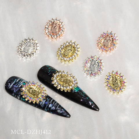 A close-up showcases decorative nail art pieces on a marble-like surface, where two black elongated nail tips are adorned with gold and multicolored gemstone embellishments. These striking designs feature Virgin Mary charms from the Dynamic Nail Supply product line (Small version) in a 12 pcs bag, adding a touch of spiritual elegance. Complementing these charms are oval embellishments in gold, silver, and rose gold hues with colorful gems.