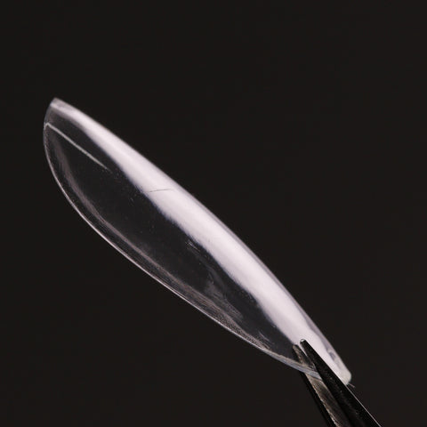 Natural Round (Medium) Soft-Gel Nail Tips, like a contact lens held by tweezers, shown against a dark background.