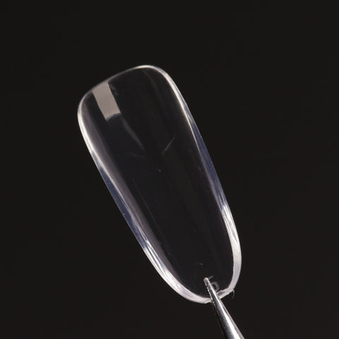 A Natural Round (Medium) Full Cover Soft-Gel Nail Tip (Pink Box) held by tweezers against a black background.