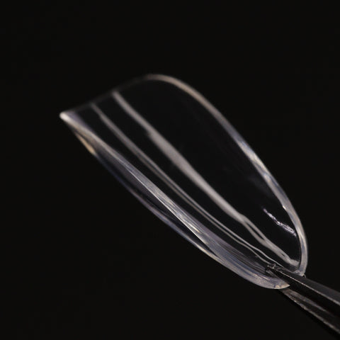 A Natural Round (Medium) Full Cover Soft-Gel Nail Tip held by tweezers against a black background.