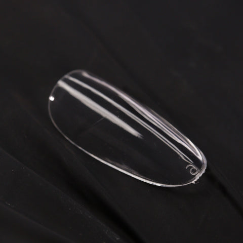 A Natural Round (Medium) Full Cover Soft-Gel Nail Tip rests on black, slightly wrinkled fabric.