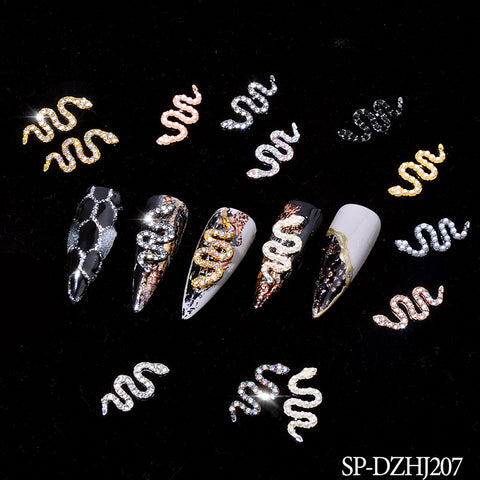 A set of five long, pointed nails showcases intricate snake designs with golden and silver glitter. Each piece is adorned with unique patterns featuring black scales, shiny gold snakes, and contrasting textures. The nail art is further elevated by small metallic snake shape charms in various colors from the 10 pcs of Snake Shape Charms for Nails Art Design (Smaller version) by Dynamic Nail Supply.