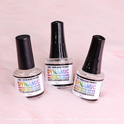 Three bottles of Dynamic Nail Supply's Dynamic Protein Bond - Professional Non-acid Bonding for Preps are elegantly displayed against a soft pink background. The labels on the clear glass bottles read "Dynamic Protein Bond" in colorful text. Designed to prevent nail lifting, each bottle features a black cap, emphasizing its ability to create a sticky surface.