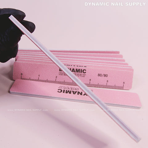 A gloved hand holds a Square Nail File 80/80 Coarse above pink buffers, double-sided, from DYNAMIC NAIL SUPPLY.