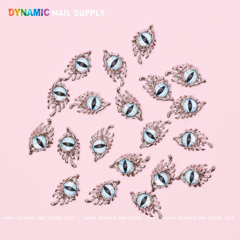 The image showcases a collection of 23 metallic, eye-shaped nail art charms called "The Light Blue GreaT EyEs (Eye of SauR0n)", featuring a vibrant blue iris and intricate lashes, encased in silver frames. They are arranged on a light pink background with "Dynamic Nail Supply" prominently displayed at the top left, accompanied by their website below.