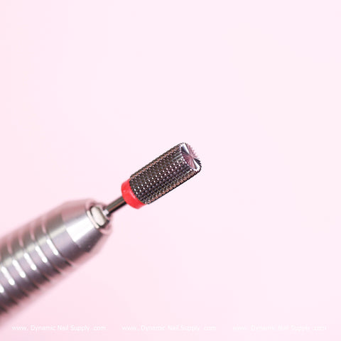 A close-up of the Safety Barrel Bit by Dynamic Nail Supply showcases its silver texture with a textured cylindrical head and a distinctive red band near the tip, making it ideal for smoothing out acrylic and sealing cuticles. Set against a soft pink background, this fine grit drill bit is frequently used in nail salons for shaping and smoothing nails during manicures and pedicures.