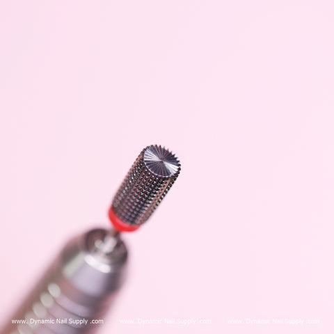 A close-up view showcases the Safety Barrel Bit (new) Fine grit by Dynamic Nail Supply against a pale pink background. This cylindrical metal bit, perfect for smoothing acrylics and sealing the cuticle, is attached to a drill tool. A distinctive red band encircles the bottom of the bit, while www.DynamicNailSupply.com scrolls repeatedly at the bottom.