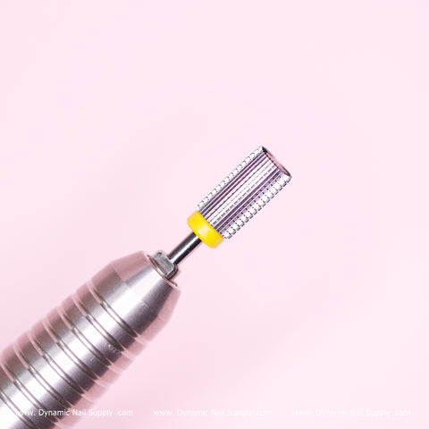 Close-up of a silver cylindrical nail drill fitted with the new Super Fine Barrel Bit by Dynamic Nail Supply, featuring an extra fine grit for smooth cuticle sealing and a textured metallic tip with a yellow band. The soft pink background complements the faint words "Dynamic Nail Supply" along the bottom edge, highlighting its precision in cuticle care.