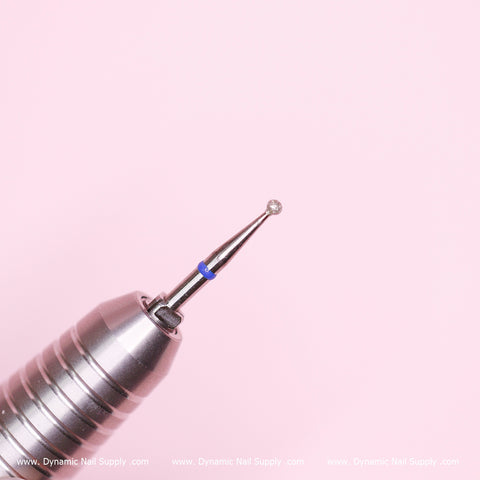 In the foreground is a close-up of a metallic Medium Cuticle Drill Bit by Dynamic Nail Supply, featuring a 1.85mm diameter spherical tip ideal for cleaning cuticles and removing dead skin. A blue band marks the base of the bit, against a soft pink backdrop. The website www.DynamicNailSupply.com is displayed in white text along the bottom edge.