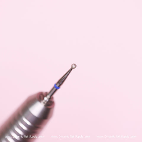 A close-up view of the Medium Cuticle Drill Bit, featuring a silver diamond design with a rounded tip, is set against a soft pink backdrop. This 1.85mm diameter ball bit is perfect for cleaning the cuticle area and removing dead skin, showcasing intricate metallic detailing as its focal point. The brand name, Dynamic Nail Supply, is subtly visible at the bottom in small, white font.
