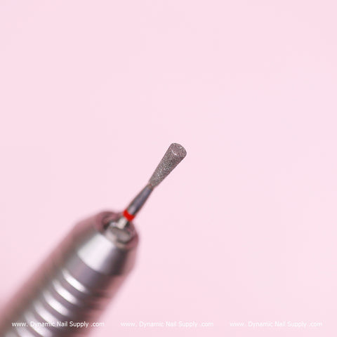 Close-up of a cylinder-shaped drill bit from Dynamic Nail Supply against a pink background. The textured metallic tip is ideal for precision in cleaning the cuticle area, while the cylindrical handle features grooves for improved grip. A Dynamic Nail Supply watermark at the bottom of the image assures authenticity and quality.