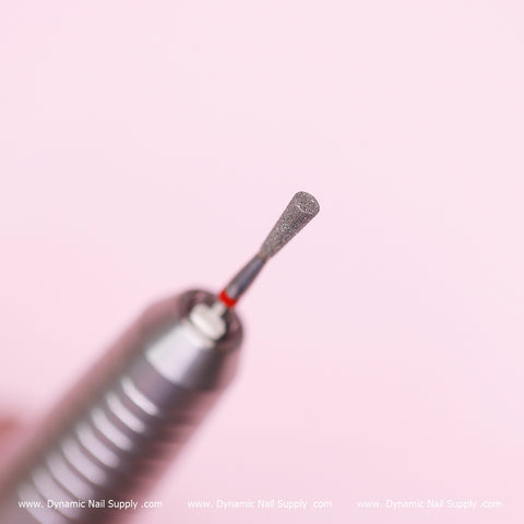 A close-up view of a Cylinder-shaped Drill Bit (Fine - Russian Manicure) against a pink background. The metal bit features a textured surface, ideal for prepping, cleaning the cuticle area, and removing dead skin. The branding www.DynamicNailSupply.com is prominently displayed at the bottom, emphasizing the source and brand name: Dynamic Nail Supply.