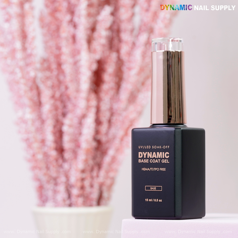 Dynamic No-HEMA Base Coat Gel (black bottle, silver cap) shown with pink dried flowers on a light surface.