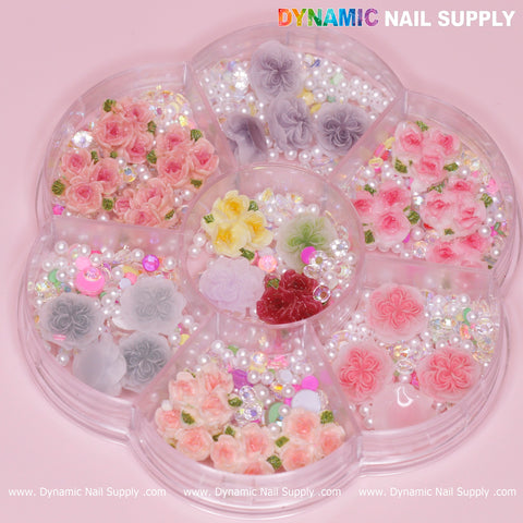 The Dynamic Nail Supply wheel presents a collection of 40 pieces of white and pink 3D and 5D rose flower charms adorned with small pearls, set against a pastel pink background. This arrangement offers vibrant floral embellishments in shades of pink, yellow, red, gray, and white, ideal for Valentine nails art design.