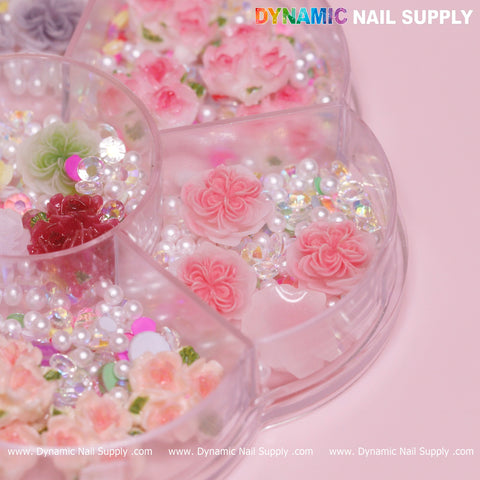 A close-up view of the Dynamic Nail Supply logo highlights a segmented organizer filled with nail art accessories, featuring sections adorned with white and pink 3D and 5D rose flower charms, pearl beads, and iridescent sequins. This set is ideal for creating Valentine nails art designs.