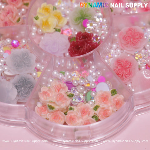 Close-up of a container featuring 40 pieces of White and Pink 3D/5D Rose Flower Charms with pearls for Valentine Nails Art Design. The pink and red roses are beautifully mixed with yellow and white blooms, complemented by small pearls and iridescent accents. This charming accessory set is from Dynamic Nail Supply, resting on a soft pink surface.