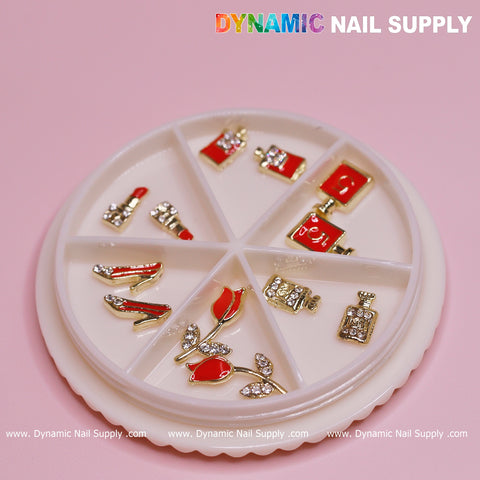 A round display case with six compartments elegantly showcases the gold and red 12 pcs Valentines Nail charms from Dynamic Nail Supply. The collection features dazzling designs like lipstick, high heels, perfume bottles, roses, and handbags, all adorned with rhinestones. "Dynamic Nail Supply" is prominently displayed at the top, attracting nail designers to explore their website below.